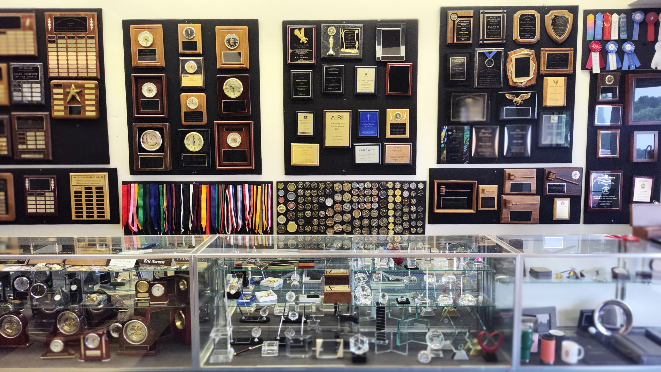 a display wall and case filled with plaques, clocks, pen sets, and more